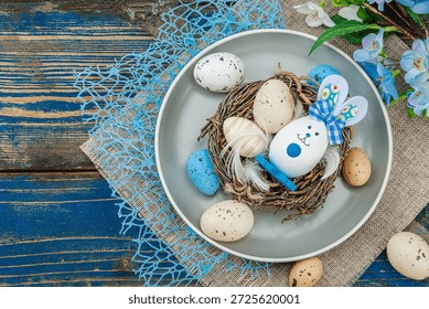Easter table setting with eggs, bird's nest and blooming branch. Traditional festive symbols, greeting card, flat lay. Old wooden boards background, top view