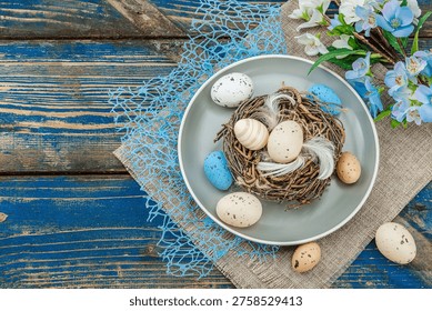 Easter table setting with eggs, bird's nest and blooming branch. Traditional festive symbols, greeting card, flat lay. Old wooden boards background, top view