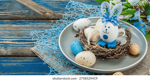Easter table setting with eggs, bird's nest and blooming branch. Traditional festive symbols, greeting card, flat lay. Old wooden boards background, banner format