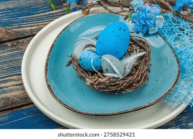 Easter table setting with eggs, bird's nest and blooming branch. Traditional festive symbols, greeting card, flat lay. Old wooden boards background, close up