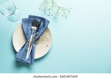 Easter table setting on blue. White plate, cutlery, easter eggs and flowers.