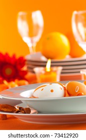 Easter table setting in orange tones with candles and flower.
