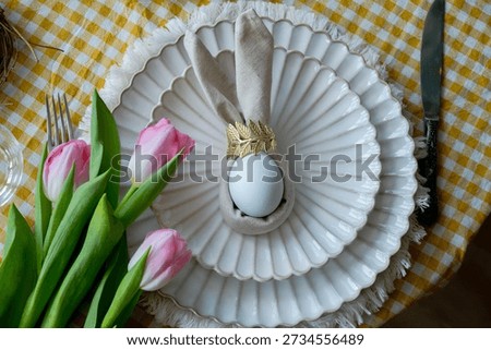 Easter table setting with spring flowers. Festive dinner. Plate with Easter egg wrapped in napkin shaped like bunny ears.
