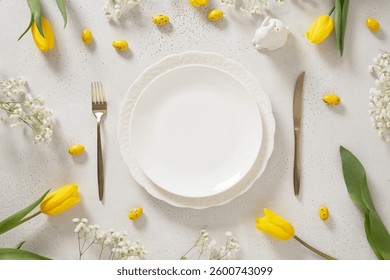 Easter table setting with spring, yellow tulips, empty white plates, bunny, eggs on white background. Happy Easter celebration. Copy space. View from above.