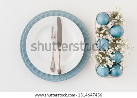 Easter table settings blue white plate, blue natural colored easter eggs in tray with small white flowers baby breath gypsophila. Easter decoration