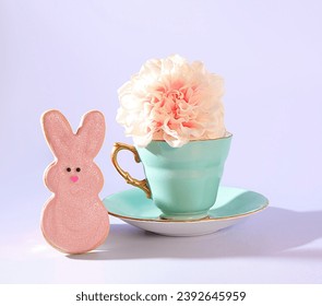 An Easter Tea Celebration: A Pastel Green Teacup with Gold Handle, a Pink Flower, and a Easter Bunny Rabbit Pink Sugar Cookie on a Pastel Purple Background - Powered by Shutterstock