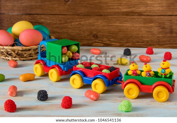 Easter toy car with trailer and color\
sweets in, Easter eggs and candy on wooden\
background