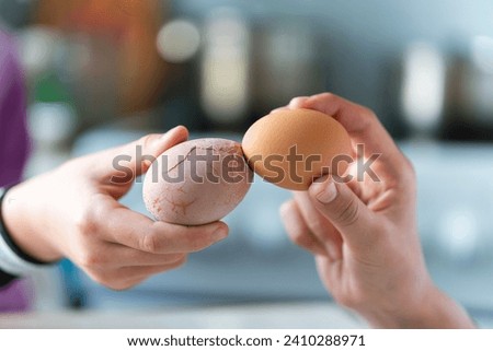 Easter tradition of cracking eggs, two hands hold eggs and try to break each other's egg, close up against blue background