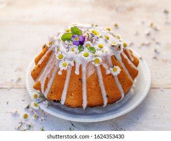 Easter yeast cake (Babka) covered with icing and decorated with edible flowers on a white plate on a white wooden table. Traditional Easter cake in Poland - Powered by Shutterstock