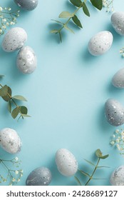 Стоковая фотография: Easter-inspired vertical top view layout in a photograph of slate greyish eggs, gypsophila, and eucalyptus artfully placed on a pastel blue surface, with a blank area for copy