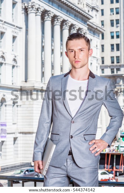 Eastern European Business Man working in New York.\
Wearing gray fashionable suit, carrying laptop computer, graduate\
student standing by vintage office building on campus. Color\
filtered effect