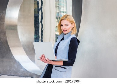 Eastern European Business Woman Working At High Tech Firm In New York, Wearing Long Vest, Black Undershirt, Leaning Back On Metal Structure, Working On Laptop Computer. Color Filtered Effect
