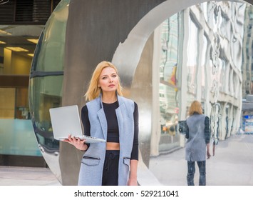 Eastern European Business Woman Working In New York, Wearing Long Vest, Black T Shirt, Standing By Metal Mirror, Working On Laptop Computer, Reading, Thinking.
