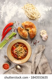 The Eastern Uzbek Cuisine. Lagman With Lamb, Noodles, Vegetables,sauce, And  Tandoor Bread. Chili Pepper, Garlic, Flour, Spoon On Gray Background. Background Image, Copy Space. Flatlay, Top View