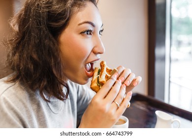 Eastern Woman Eating Sandwich Indoors At Cafe