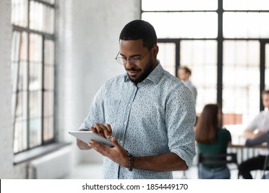 Easy Communication. Busy Concentrated Young Black Male Employee Manager Corporate Worker Standing At Office Open Space Focused On Tablet Pc Screen Accepting Urgent Order Reading Email Texting Answer