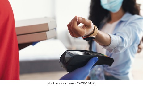 Easy Contactless Pay Concept. Closeup of delivery guy in protective gloves holding payment terminal and carton pizza boxes, woman in medical surgical face mask paying using smartwatch, selective focus - Powered by Shutterstock