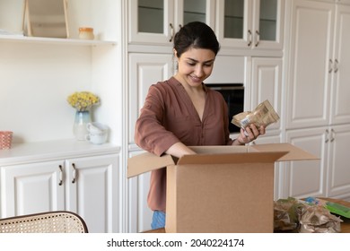 Easy food shopping. Satisfied young indian woman loyal internet market customer unpack box with groceries ordered online. Smiling mixed race lady buyer get good quality foodstuff by courier delivery