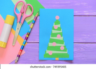 Easy Homemade Christmas Card, Scissors, Glue Stick, Pencil, Colored Paper On Purple Wooden Table. Nice Greeting Card With A Christmas Tree. Creative Idea To Make Greeting Cards From Paper. Top View