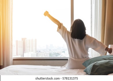 Easy lifestyle Asian woman waking up in morning weekend taking some rest, relaxing in comfort bedroom at hotel window, having a happy lazy day relaxation and enjoying work-life quality balance concept