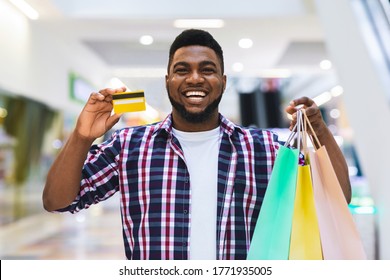 Easy Payment. Happy Black Man Holding Credit Card And Shopping Bags, Posing In Mall, Enjoying Seasonal Sales