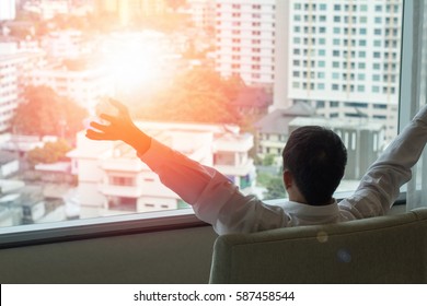 Easy relax business man lifestyle at home sitting on modern chair in living room looking out of window toward beautiful cityscape downtown urban landscape city life w/ sunlight effect: happy people - Shutterstock ID 587458544