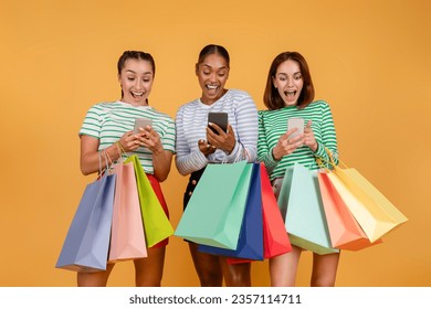 Easy shopping, black friday deal, sale season, ecommerce. Amazed happy three young multiethnic ladies shopping online, using smartphones, holding colorful shopping bags, orange background - Powered by Shutterstock
