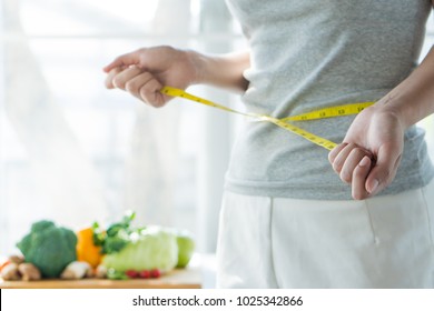 Eat good food for good shape concepts. Woman measuring her body by measure tape have a vegetables on the table as background. Girl checking her waist size down to follow up diet session result.