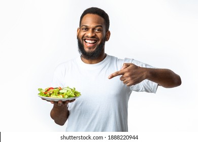 Eat Healthy. Cheerful Black Guy Pointing Finger At Plate With Vegetable Salad Dieting Standing Over White Studio Background. Male Nutrition And Weight Loss, Slimming Concept