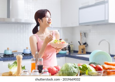 eat healthy - smiling Asian pretty female eating salad with fruits and vegetables in kitchen