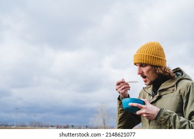 Eat Porridge With A Spoon, Bring A Cutlery To Your Mouth, A Plate Of Soup Is Held In The Hand Of A Man On A Hike, A Guy Relaxes In Nature, Has Breakfast With Food, Hot Food From A Bowl