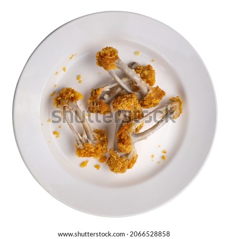 Eaten chicken wings and legs, fast food. Bones from chicken, leftovers on a plate isolated on a white background. Top view. Close-up. 
