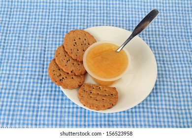 Eating Apple Sauce From Plastic Cup On White Plate With Golden Brown Cookies.