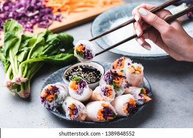 Eating Asian Cuisine Spring Rolls Or Rice Paper Rolls With Vegetables And Shrimps. Hand Holding Roll With Chopsticks