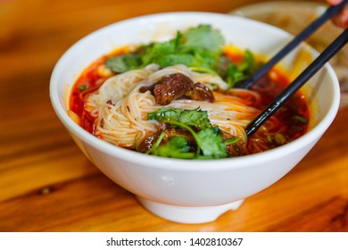 Eating A Big Bowl Of Sichuan Spicy Rice Noodle With Beef Stew On A Wooden Table