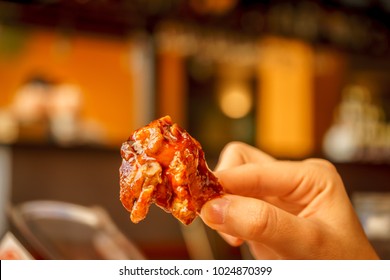 Eating Buffalo Chicken Wings With His Hands On A Blurred Restaurant Background.