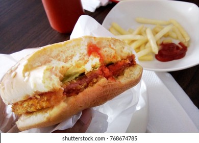 Eating Burger Sandwich, Bitten Half, Close Up. First Person View/ Hand. With Blurred Potato Chips On The Background. Fast/ American Food Concept