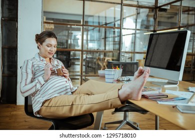 Eating Chocolate Mousse. Pregnant Woman Placing Her Legs On The Table While Eating Chocolate Mousse