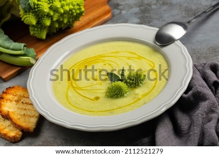 Eating creamy romanesco broccoli soup and toasted bread. Vegan dish. Fresh roman broccoli on background. Giagonal composition on dark grey surface.