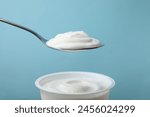 Eating delicious natural yogurt on light blue background