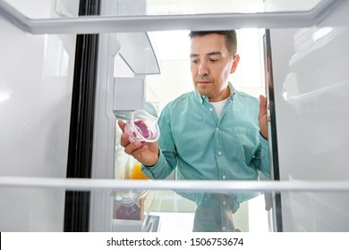 Eating And Diet Concept - Middle-aged Man Taking Container With Food Leftovers From Fridge At Kitchen