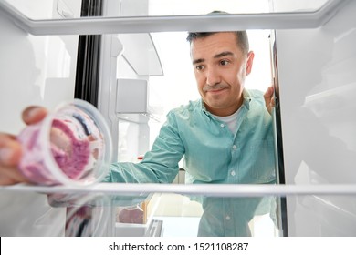 Eating And Diet Concept - Middle-aged Man Taking Container With Food Leftovers From Fridge At Kitchen