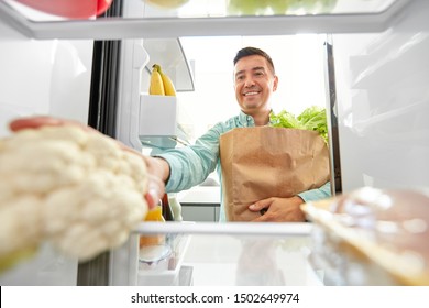 Eating, Diet And Storage Concept - Smiling Middle-aged Man With New Purchased Food In Paper Bag Putting Cauliflower To Fridge At Home