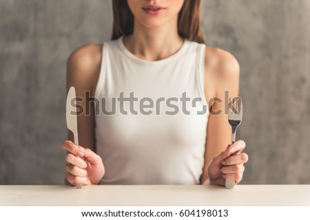 Eating disorder. Girl is sitting in front of an empty plate and holding a fork and a knife