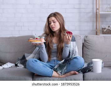 Eating disorders concept. Stressed young woman devouring sweets on couch at home, full length portrait. Unhappy lady coping with negative emotions or problems through unhealthy foods