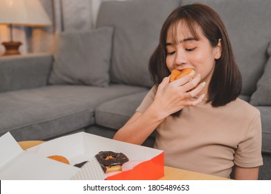 Eating donut when takeout and delivery. Fast food takeaway back home. Asian woman lifestyle in living room. Social distancing and new normal.