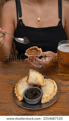 Eating empanadas at the restaurant. Closeup view of a caucasian woman having fried meat empanadas with traditional chimichurri sauce.