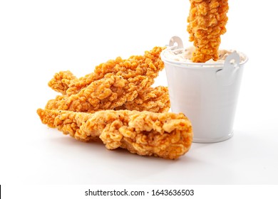 Eating Fast Food And Protein High Diet Concept With Golden Breaded Chicken Strips And One Crispy Strip Being Dipped In A Metal Bucket Of Ranch Dressing Sauce Isolated On White Background