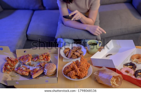 Eating Fast food when takeout
and delivery at night. Takeaway back home and watching TV. Asian
woman lifestyle in living room. Social distancing and new
normal.