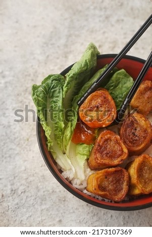 Eating fried egg chicken roll served with rice, chili sauce, and lettuce. Egg chicken roll is seasoned minced chicken wrapped inside egg-flour skin, and then deep fried.